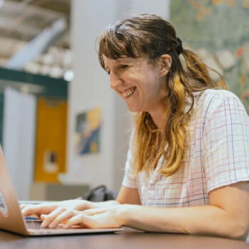 A student smiles at a computer at a desk.