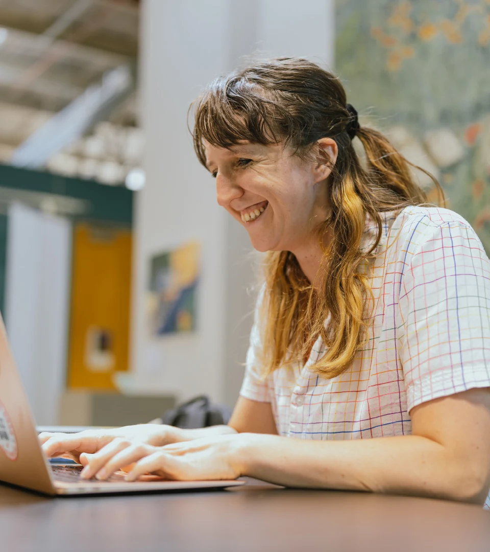 A student smiles at a computer at a desk.