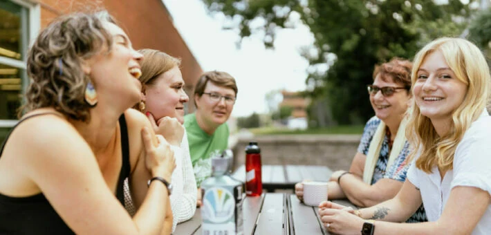 Students speak together at a table outside.