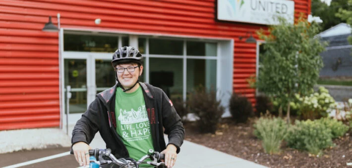 A student sits on a bike in front of the campus entrance.