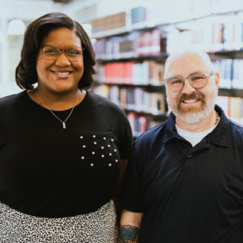 Two faculty members stand smiling side to side.