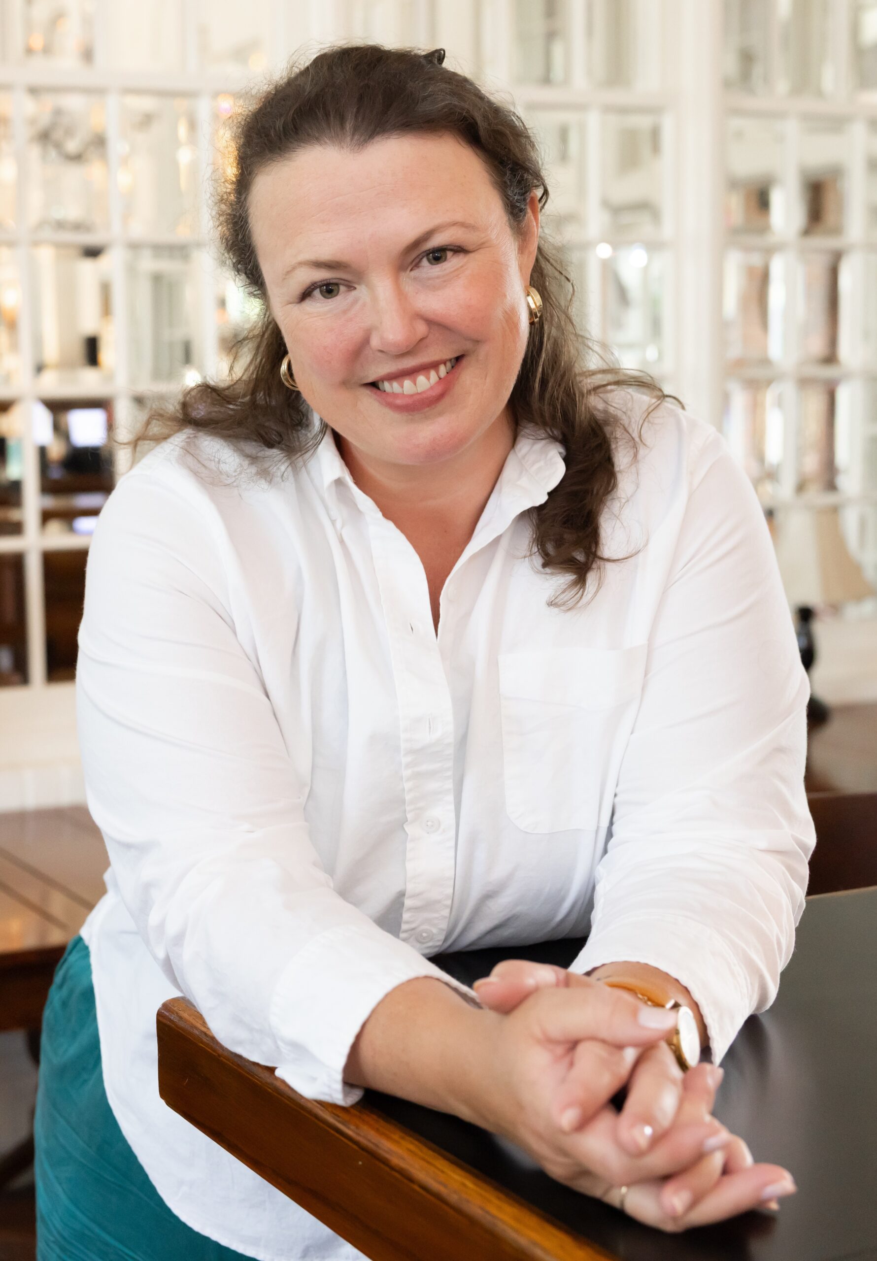 Headshot of Sarah Staiger. Leaning forward on a counter with hands clasped in front.